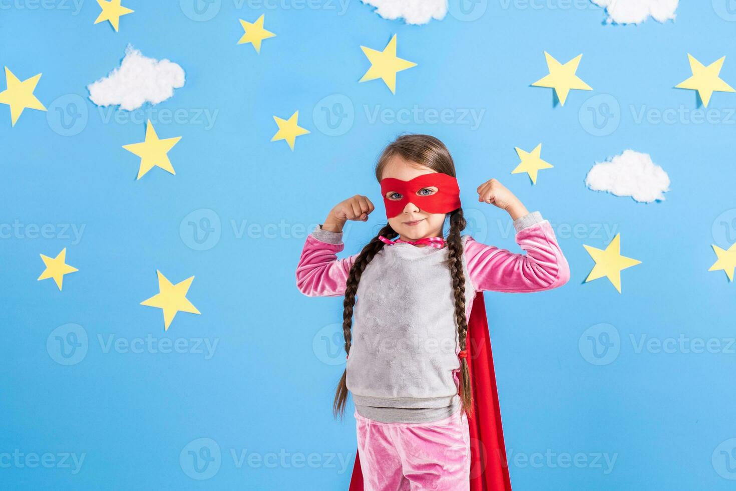 Six year blonde girl dressed like superhero having fun at home. Kid on the background of bright blue wall. photo