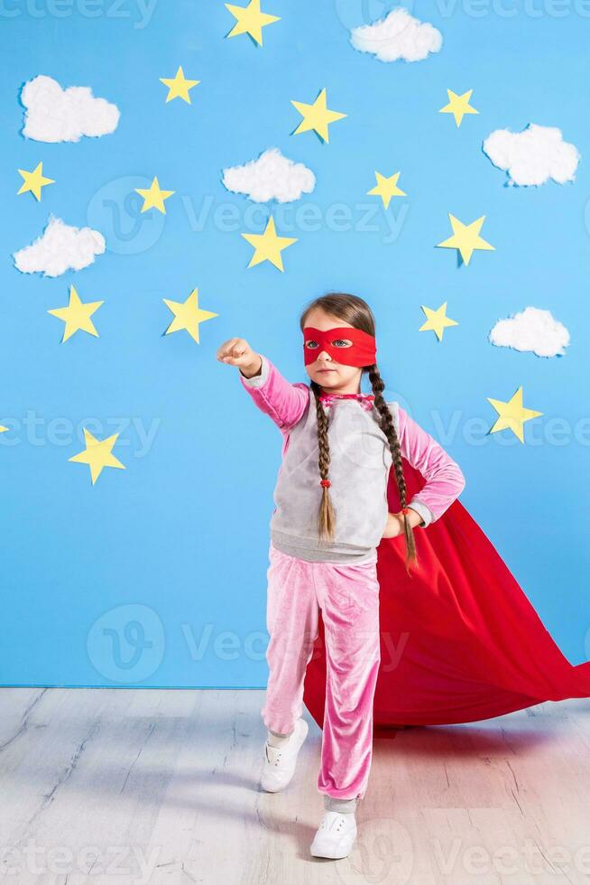 Little child plays superhero. Kid on the background of bright blue wall. photo