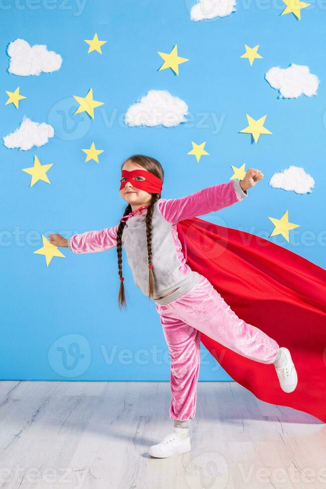 seis año rubia niña vestido me gusta superhéroe teniendo divertido a hogar. niño en el antecedentes de brillante azul pared. foto