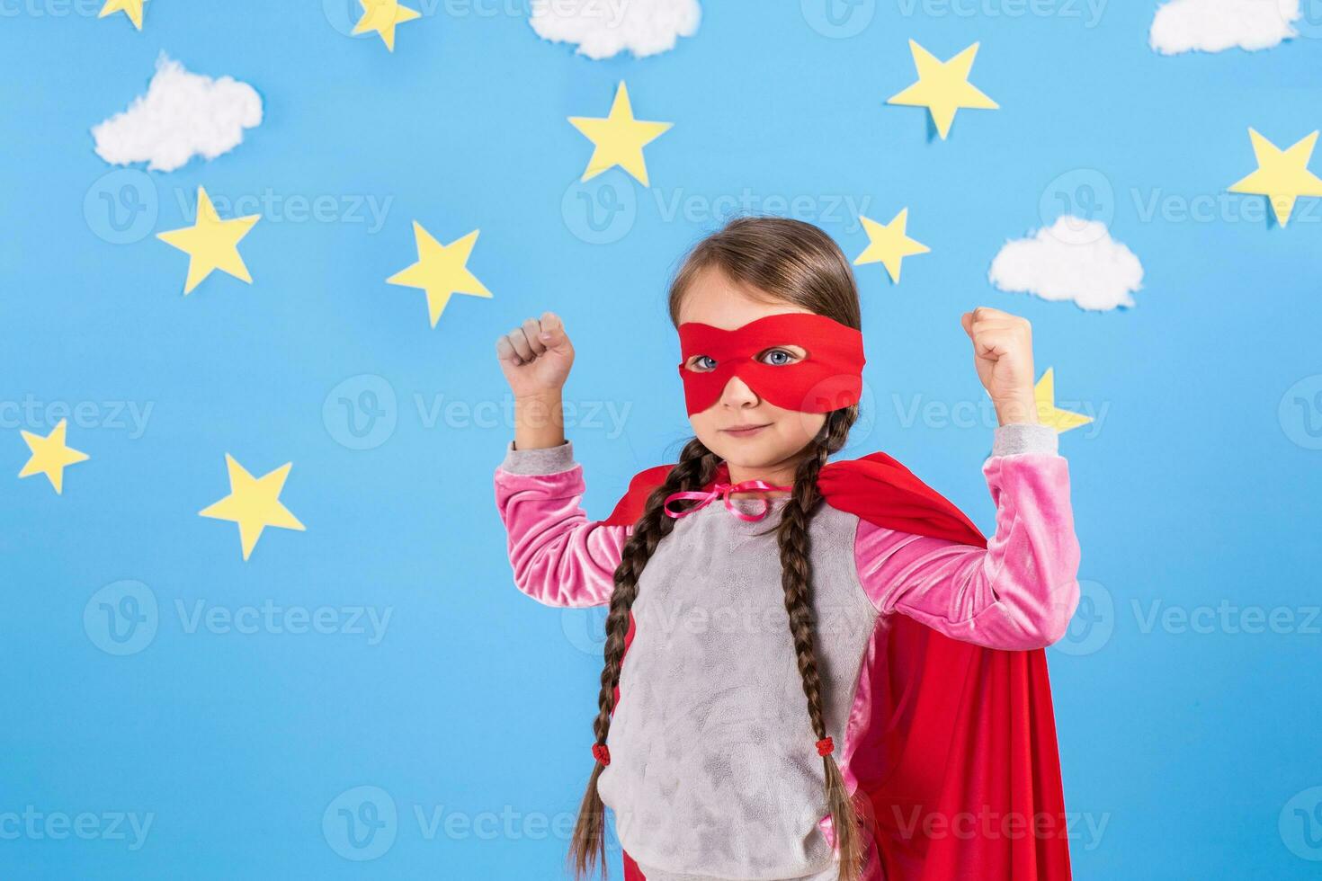 Six year blonde girl dressed like superhero having fun at home. Kid on the background of bright blue wall. photo