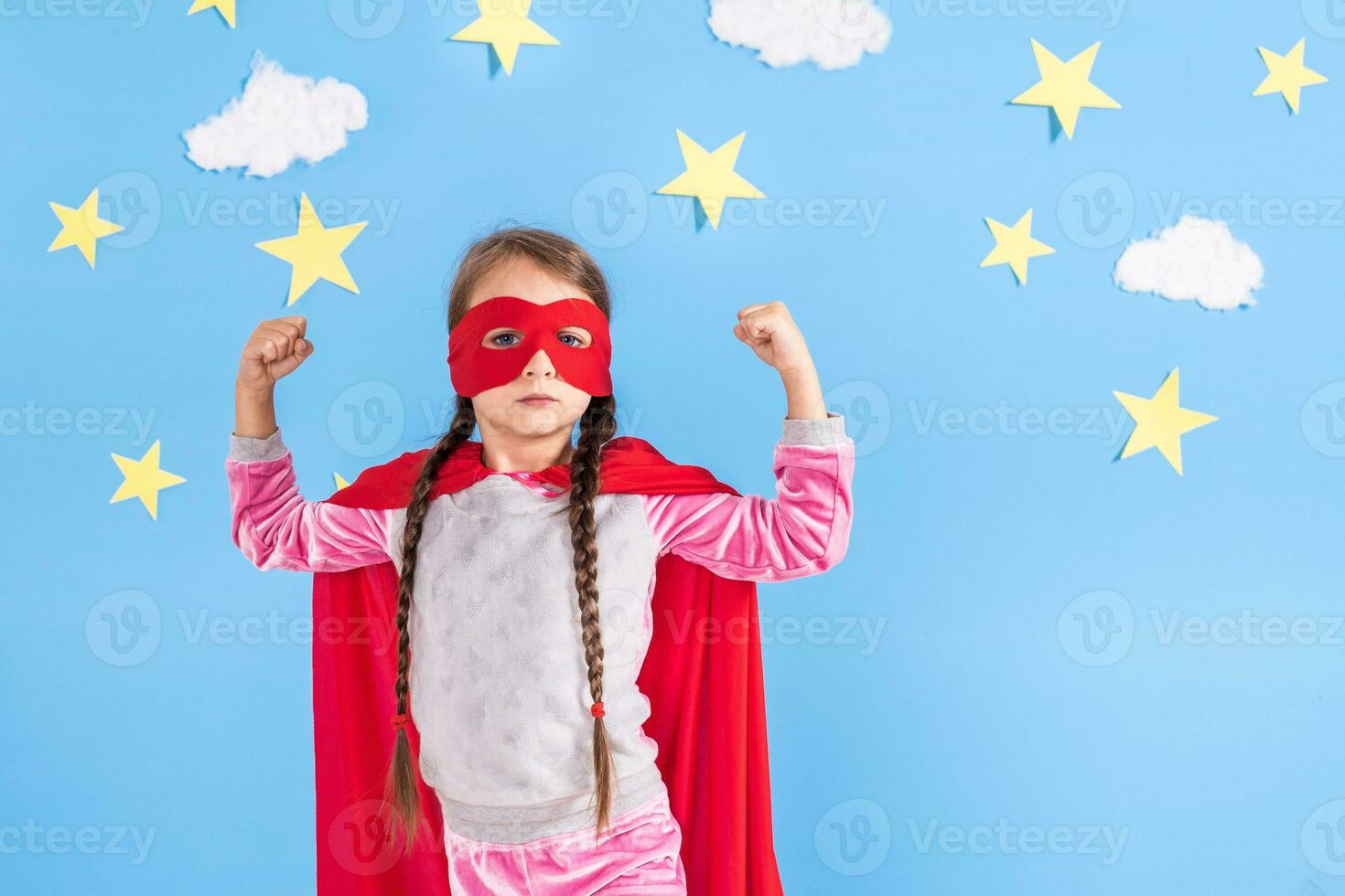 Six year blonde girl dressed like superhero having fun at home. Kid on the background of bright blue wall. photo