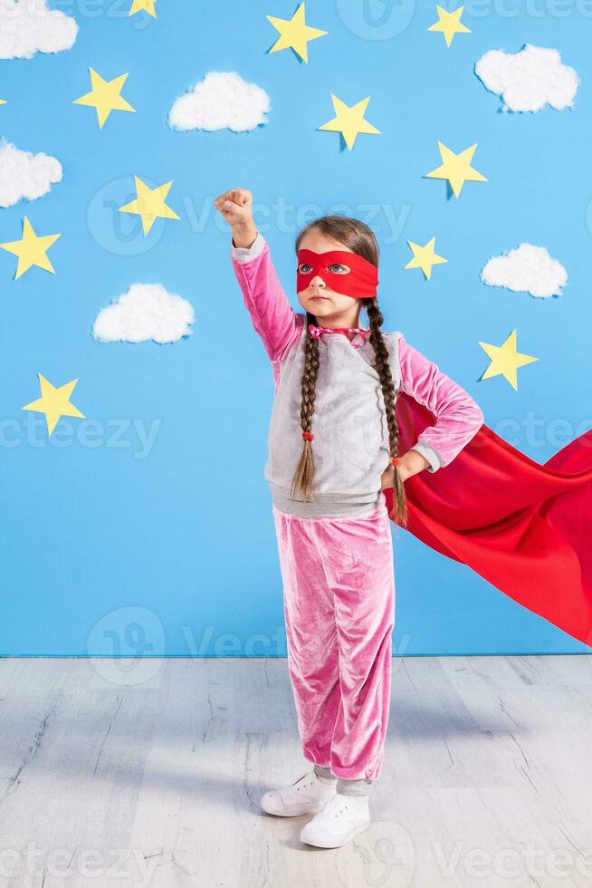 Six year blonde girl dressed like superhero having fun at home. Kid on the background of bright blue wall. photo