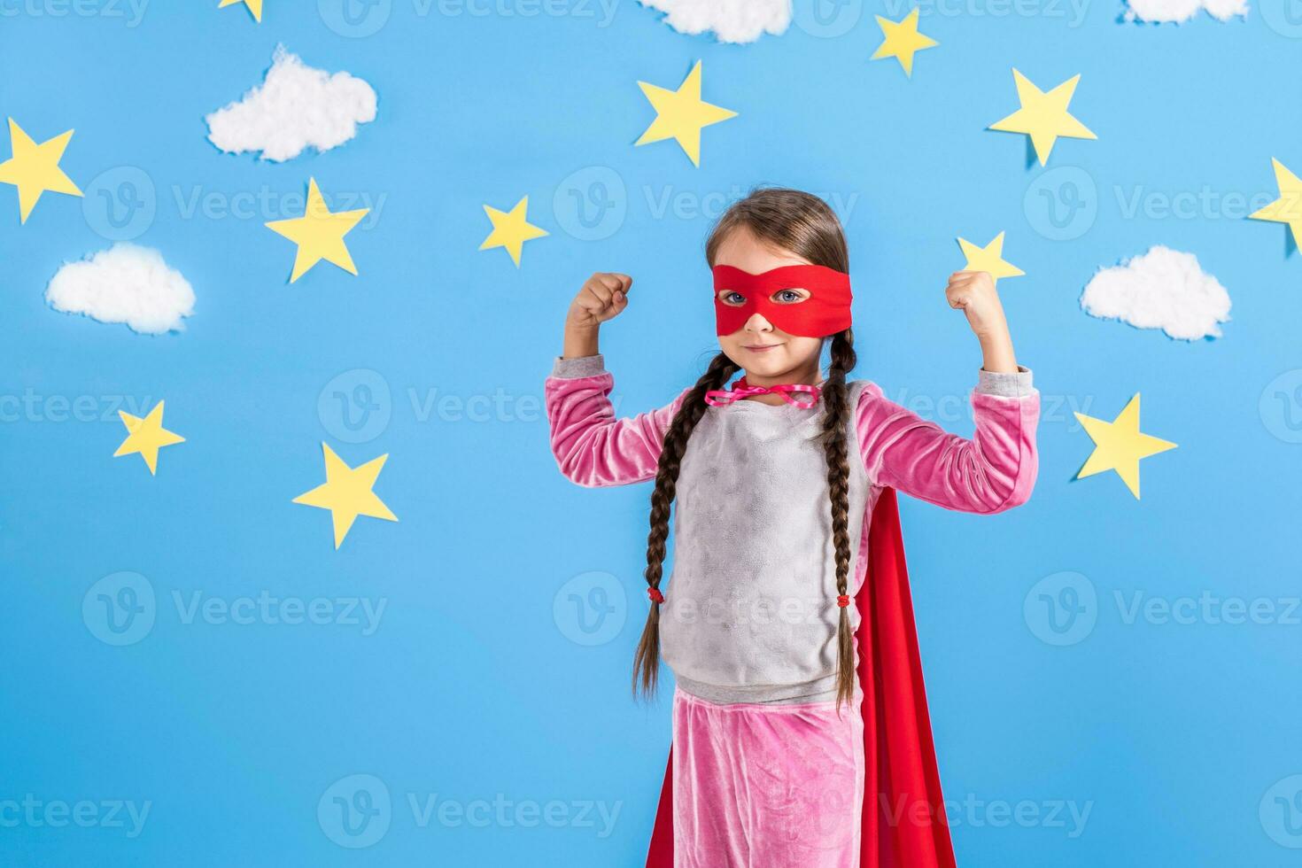 Six year blonde girl dressed like superhero having fun at home. Kid on the background of bright blue wall. photo