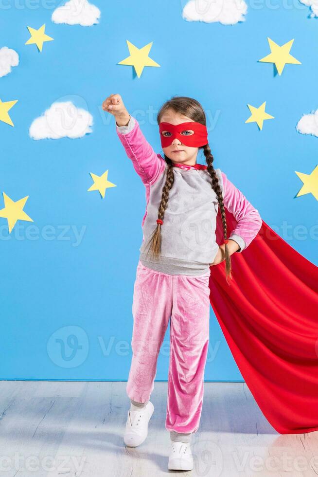 Little child plays superhero. Kid on the background of bright blue wall. photo