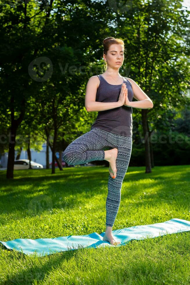 Young woman doing yoga exercises in the summer city park. photo