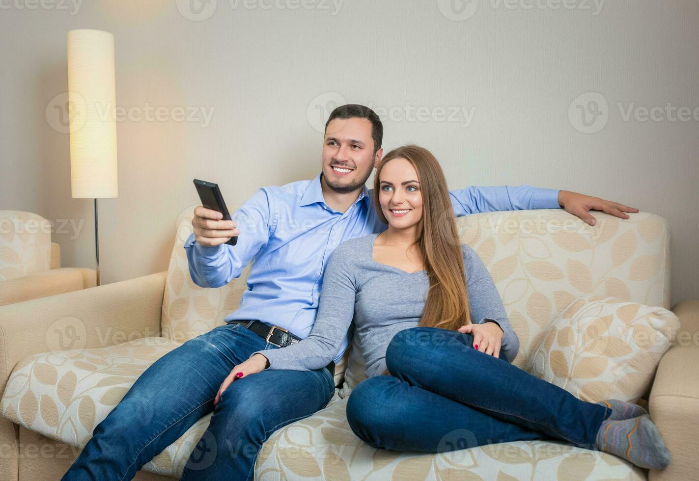 Portrait of happy couple sitting on sofa watching television together photo