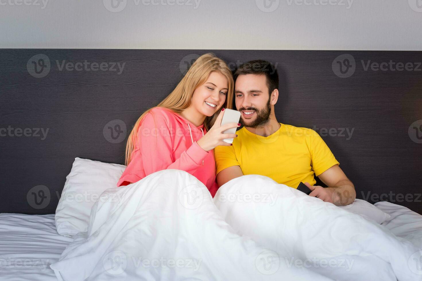 Young sweet couple in bed looking at a mobile phone photo