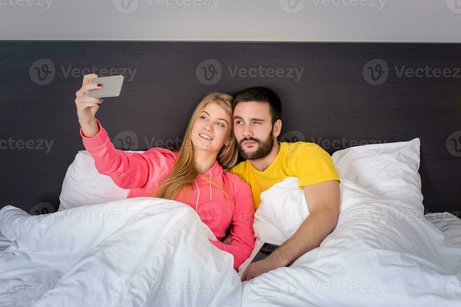 Young happy couple on bed doing selfie with telephone camera. photo