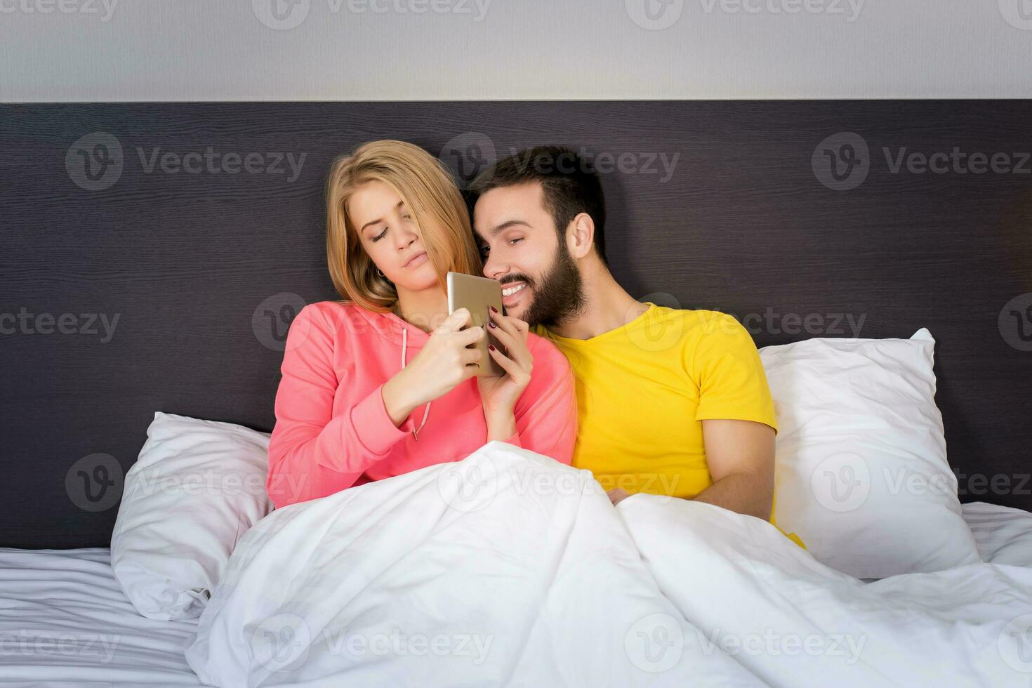 Young Sweet Couple at Bed Watching Something on Tablet Gadget photo
