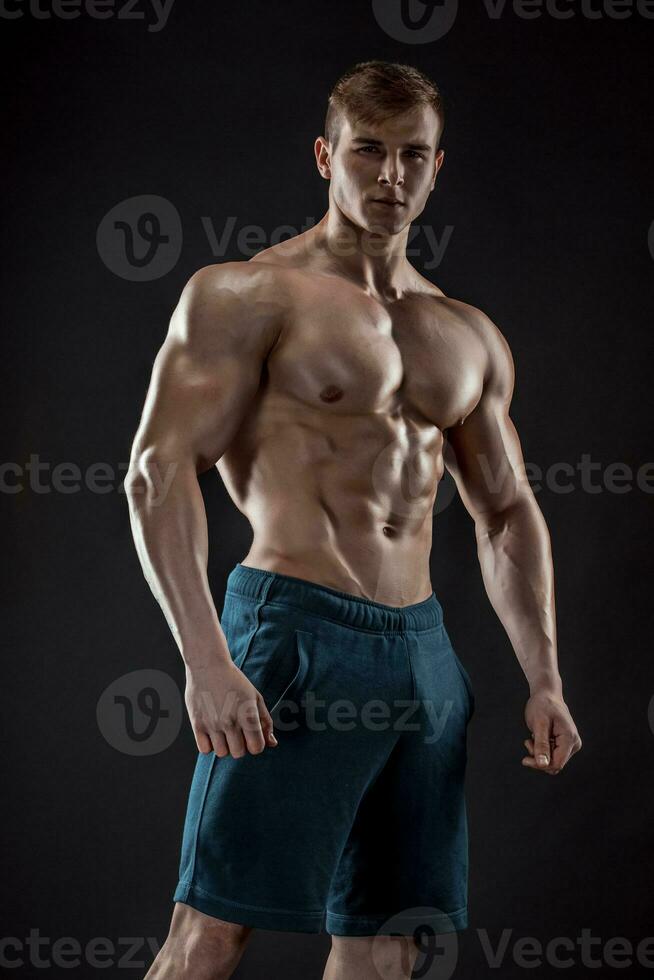 Muscular bodybuilder guy doing posing over black background photo