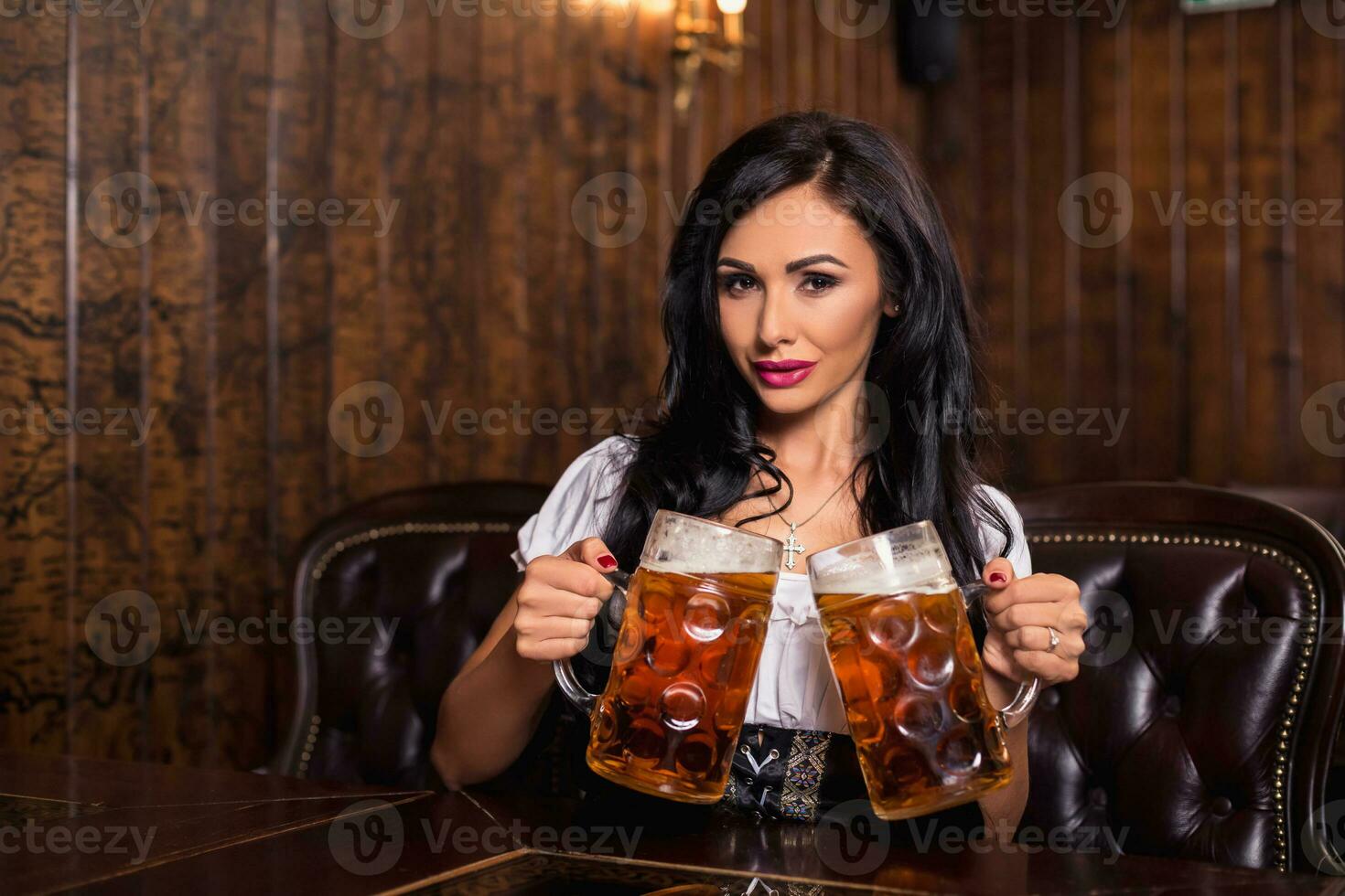 Oktoberfest woman wearing a traditional Bavarian dress dirndl posing with a beer mugs at bar photo