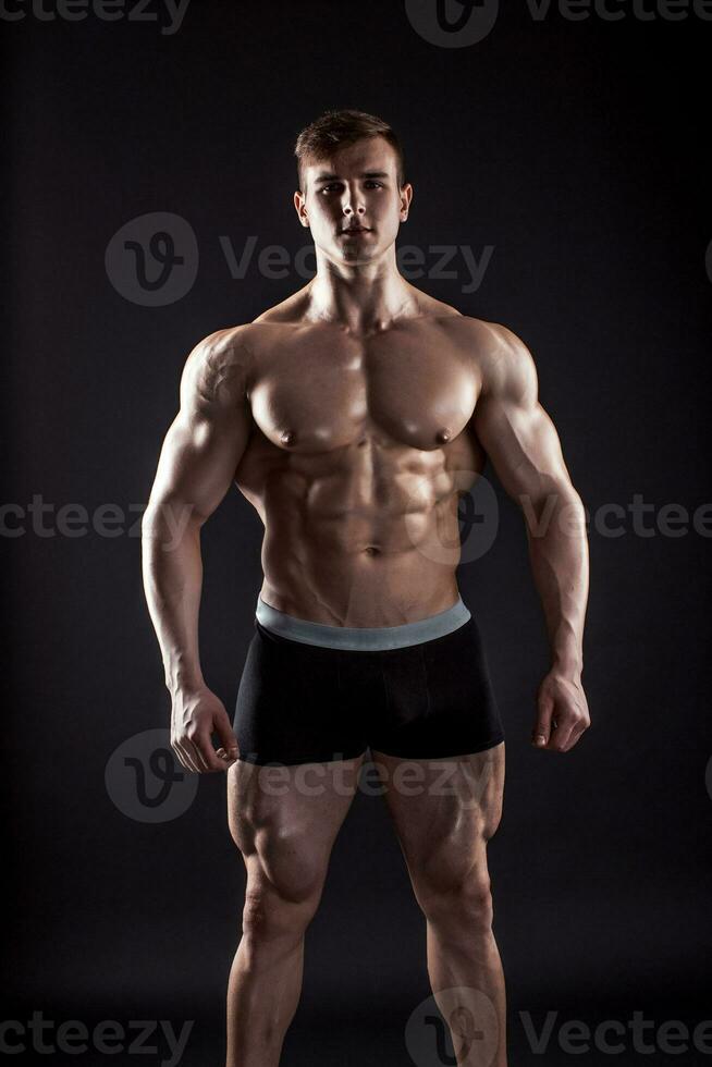 Muscular bodybuilder guy doing posing over black background photo