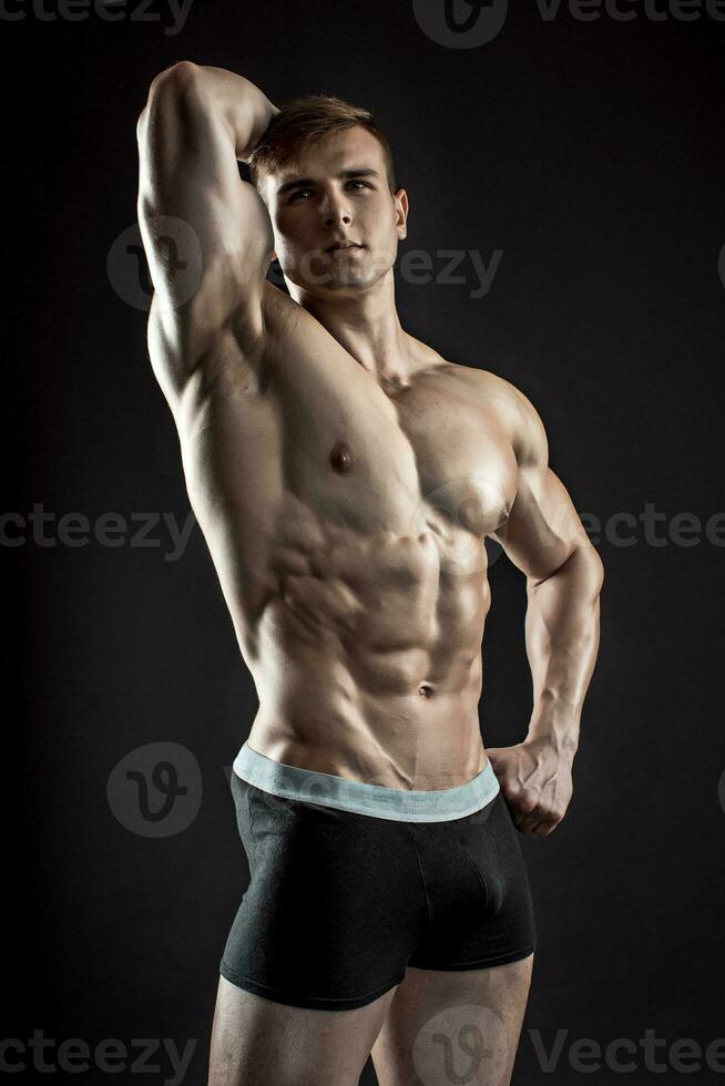 Muscular bodybuilder guy doing posing over black background photo