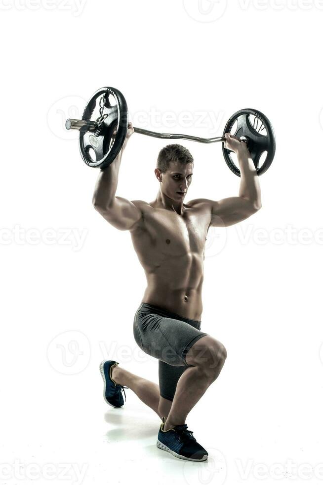 Muscular man standing on knee, holding barbell over his head photo