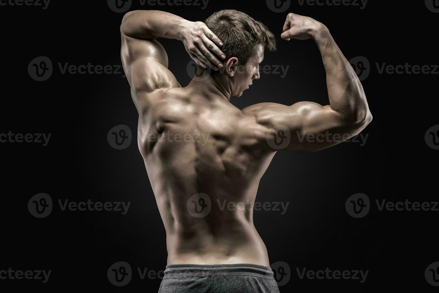 Healthy muscular young man showing back and biceps muscles photo