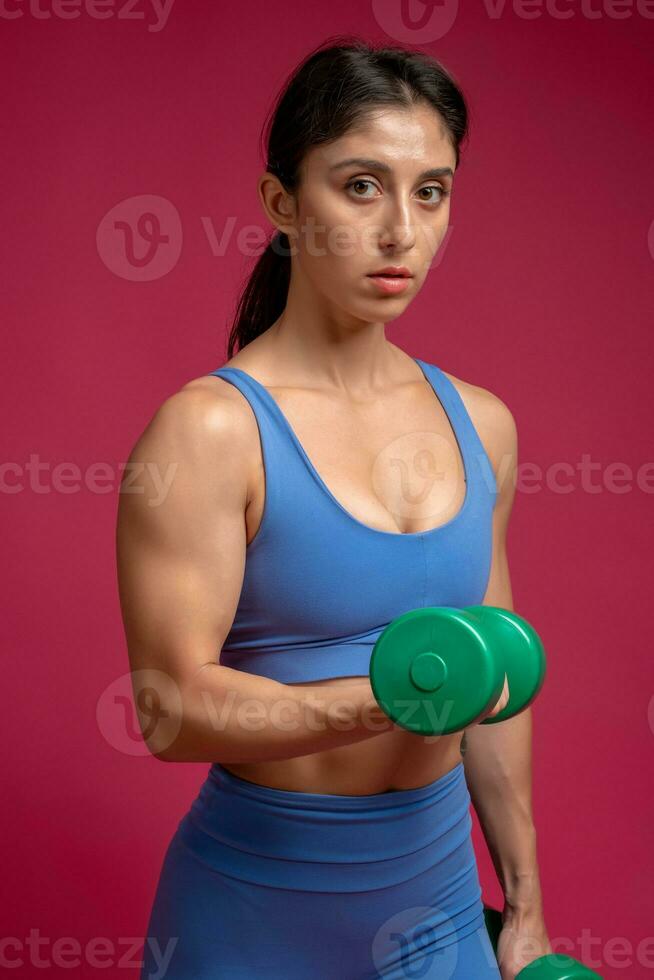 Young woman doing set of arm exercises with dumbbells on maroon background photo