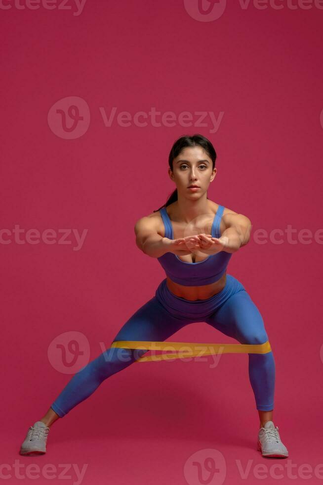 Girl doing lateral lunges with resistance band on maroon background photo