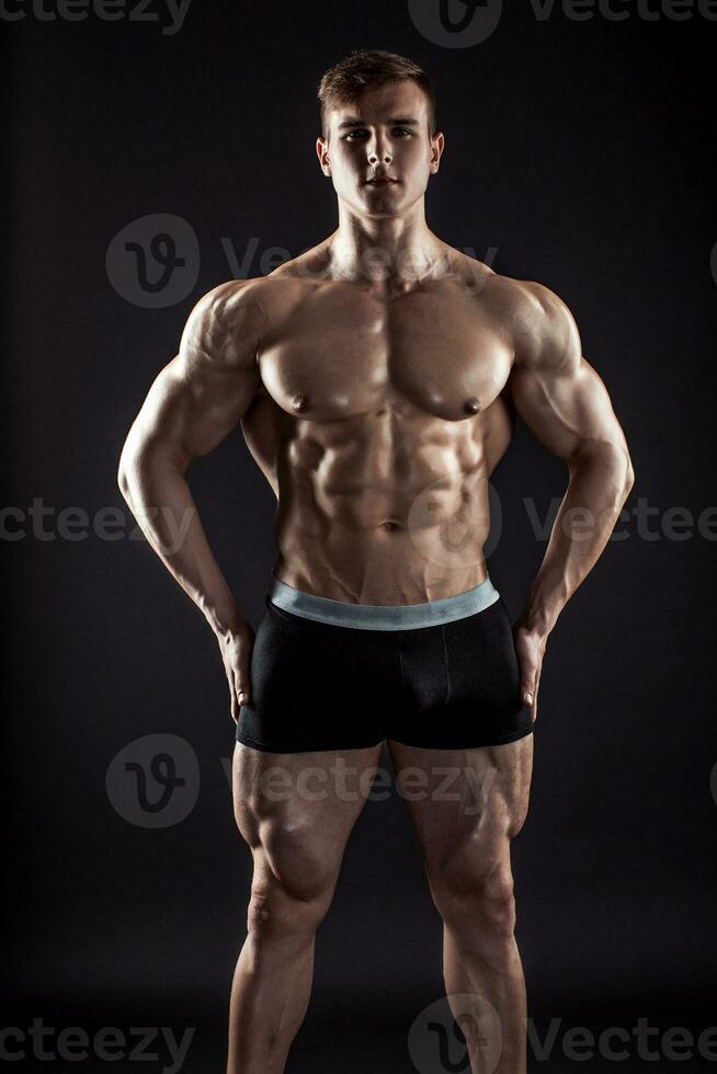 Muscular bodybuilder guy doing posing over black background photo