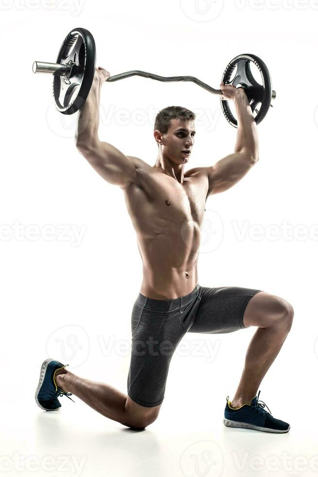 Muscular man standing on knee, holding barbell over his head photo