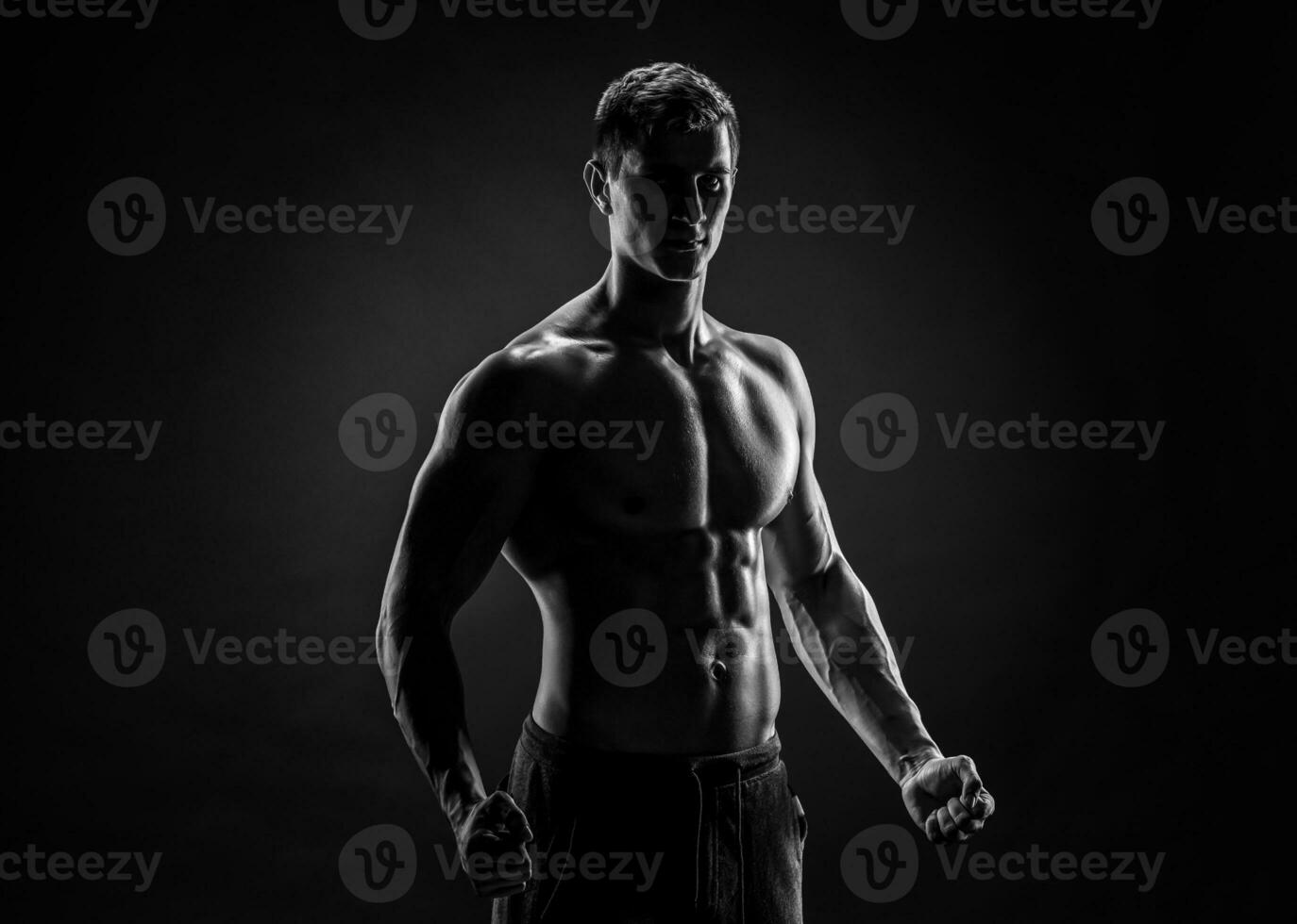 Sexy shirtless bodybuilder posing, looking at camera on black ba photo