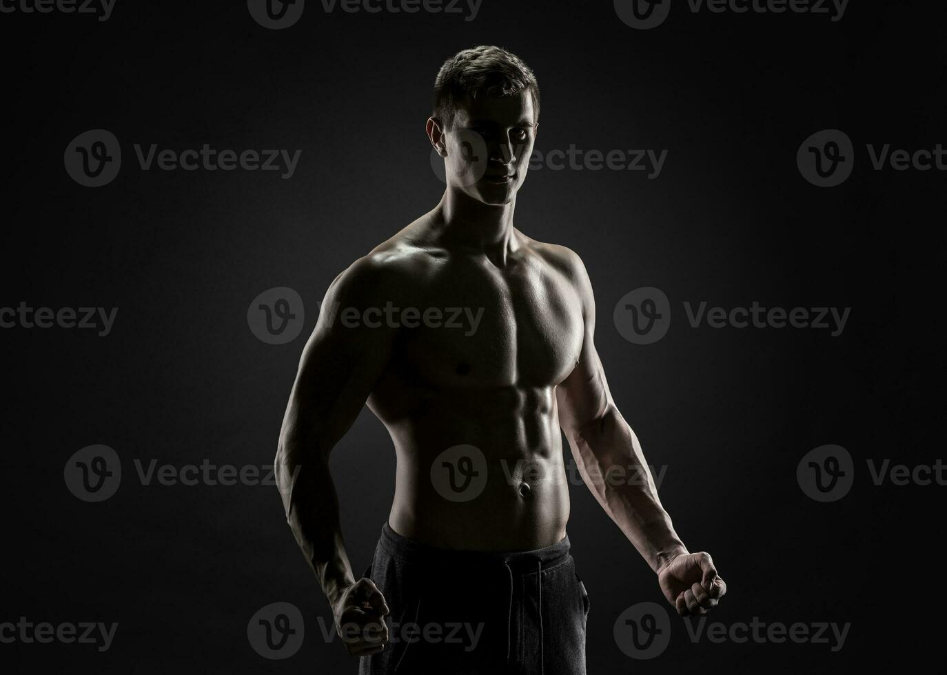 Sexy shirtless bodybuilder posing, looking at camera on black background. photo