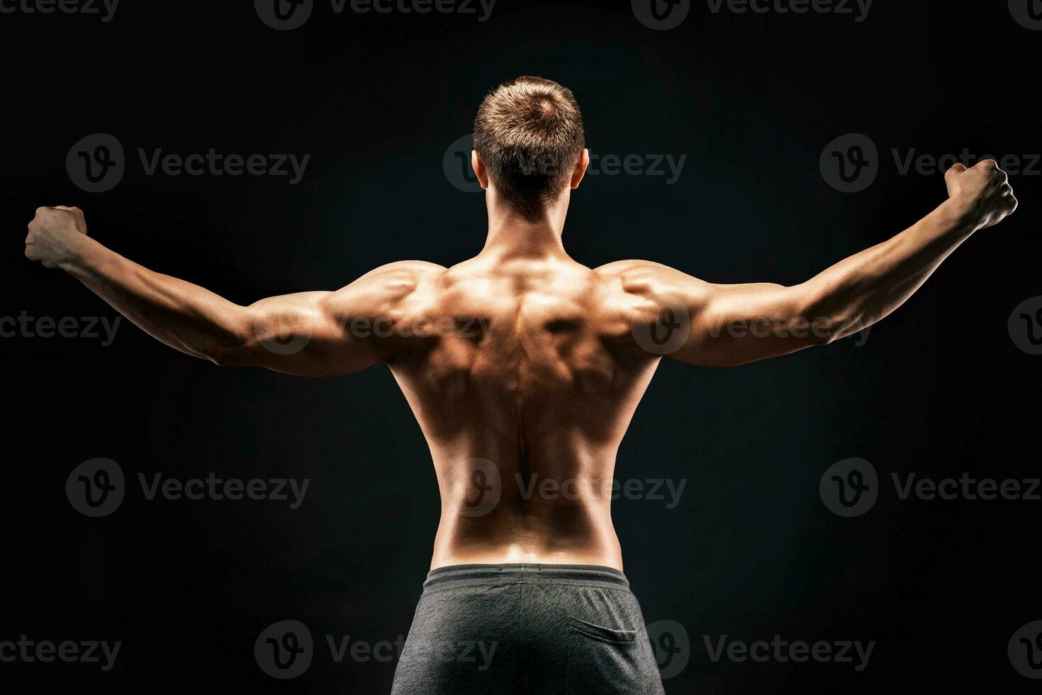Rear view of muscular young man showing back, biceps muscles photo