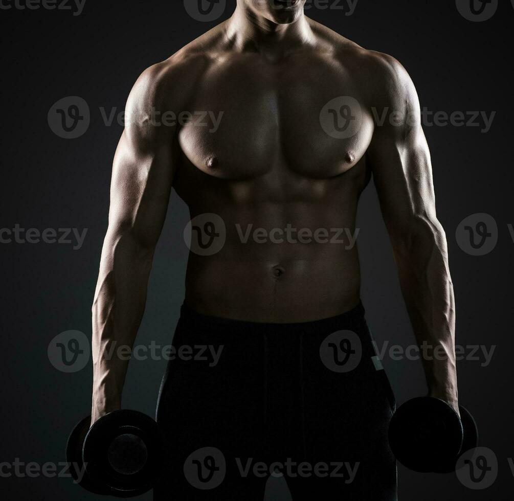 Muscular man showing perfect body with dumbbells on black background photo
