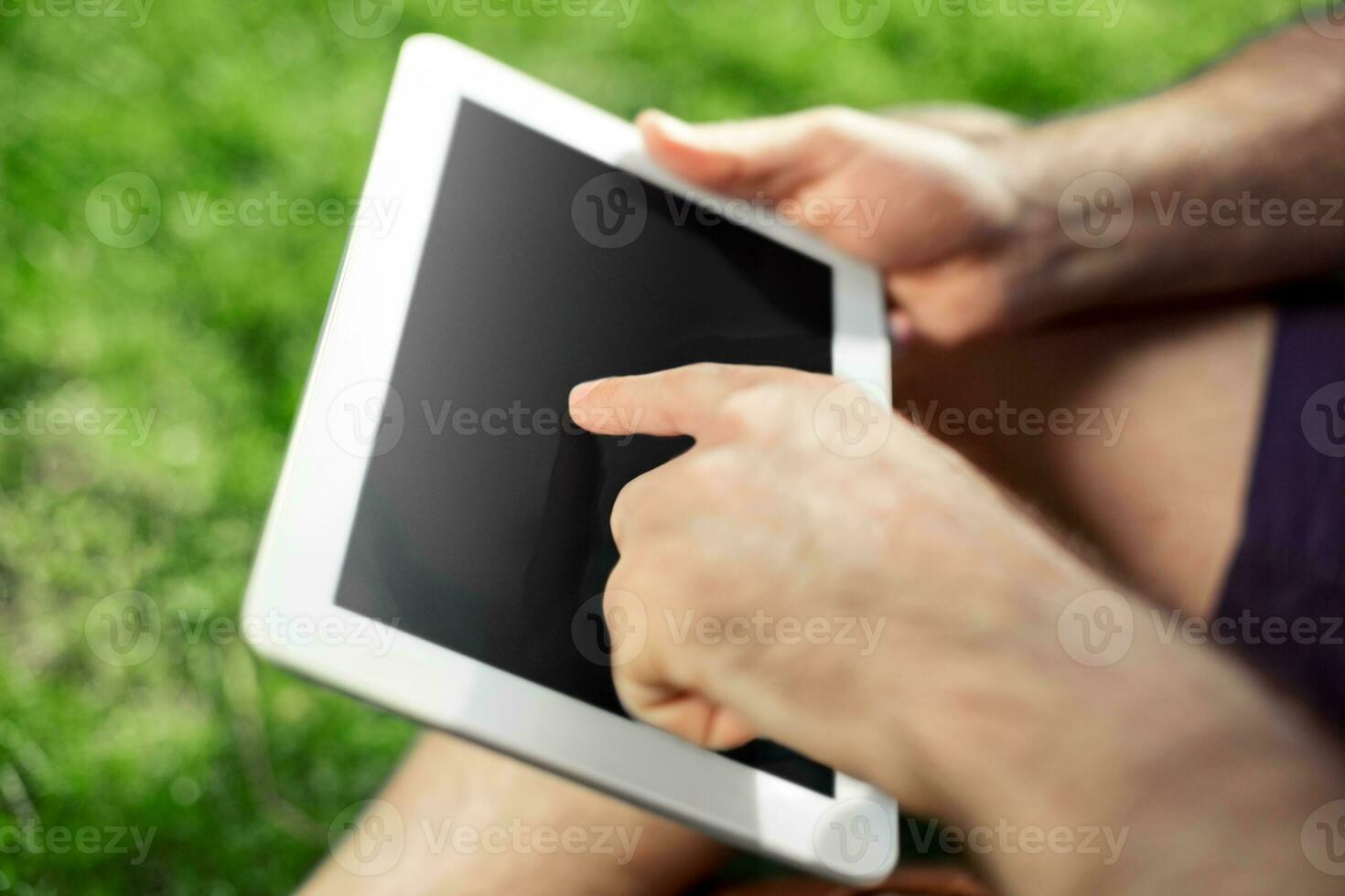 Young hipster boy sitting in the park and using modern digital tablet photo