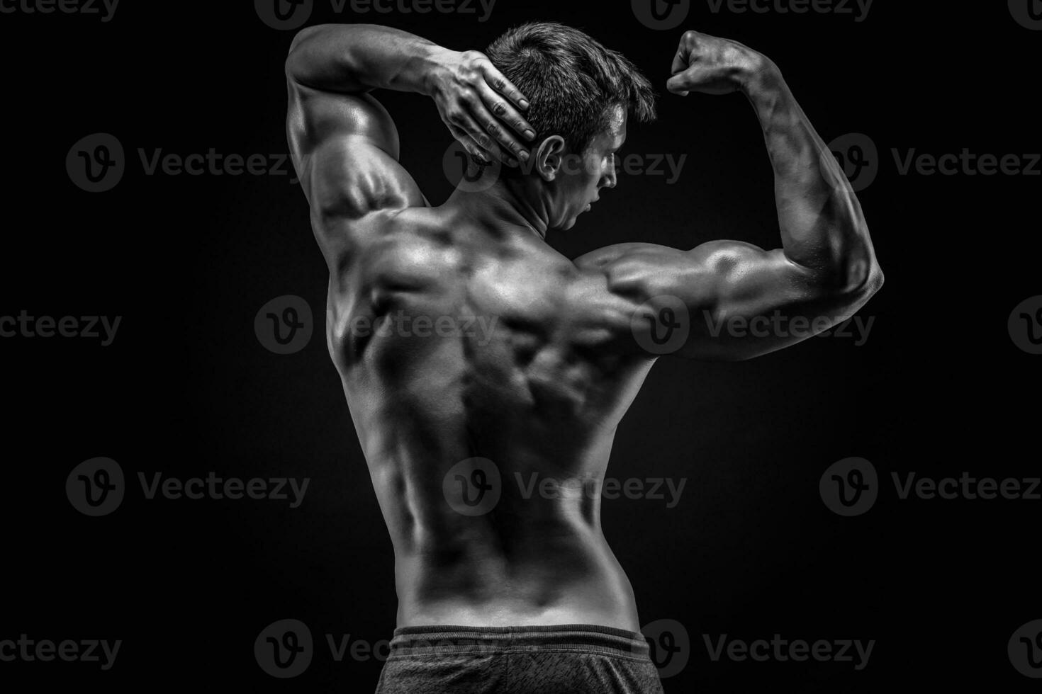 Healthy muscular young man showing back and biceps muscles photo