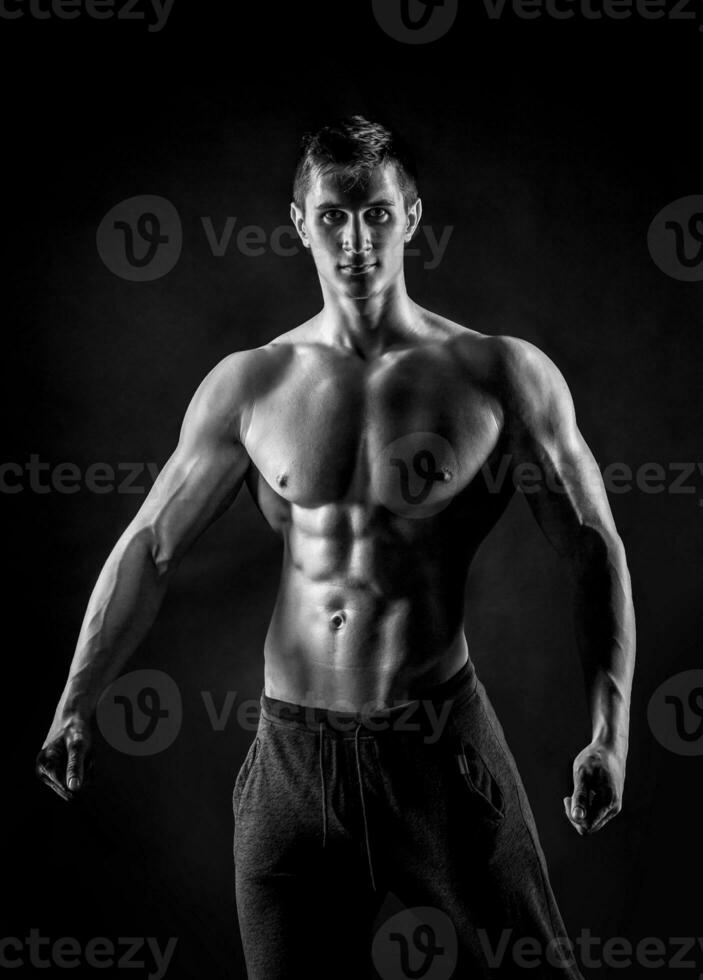 Sexy shirtless bodybuilder posing, looking at camera on black ba photo