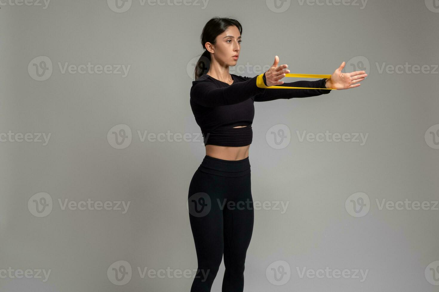 Girl doing arm and shoulder exercises with resistance band on grey background photo