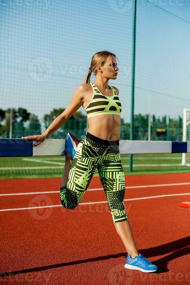 Young, beautiful girl athlete in sportswear doing warm-up at the stadium photo