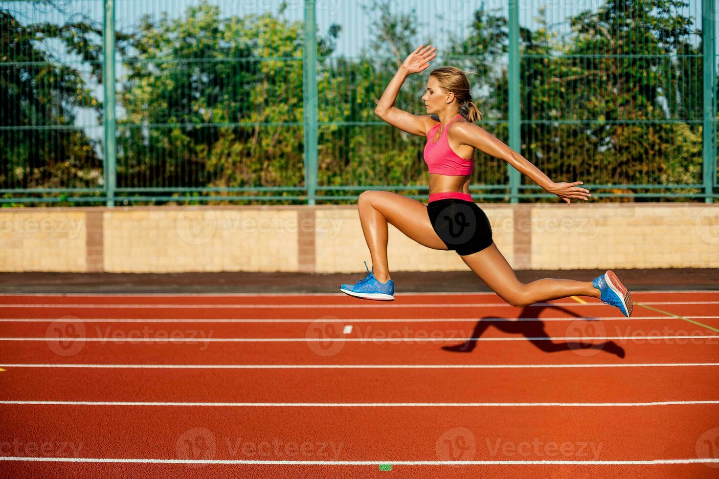 lado ver hermosa joven mujer ejercicio trotar y corriendo en atlético pista en estadio foto