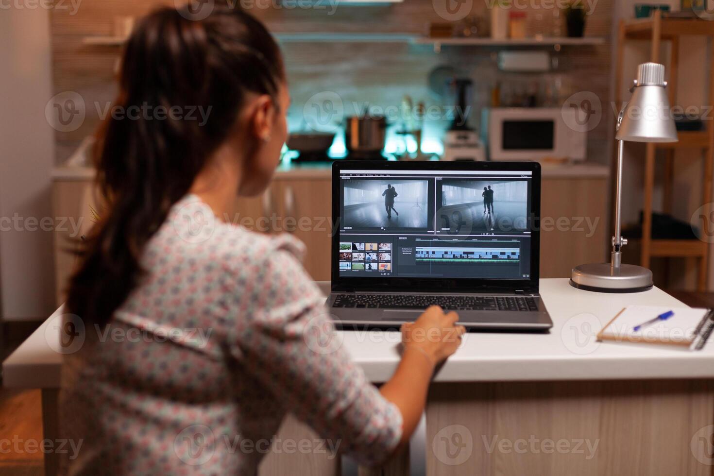 Back view of creative filmmaker working on a movie on laptop during midnight. Content creator in home working on montage of film using modern software for editing late at night. photo