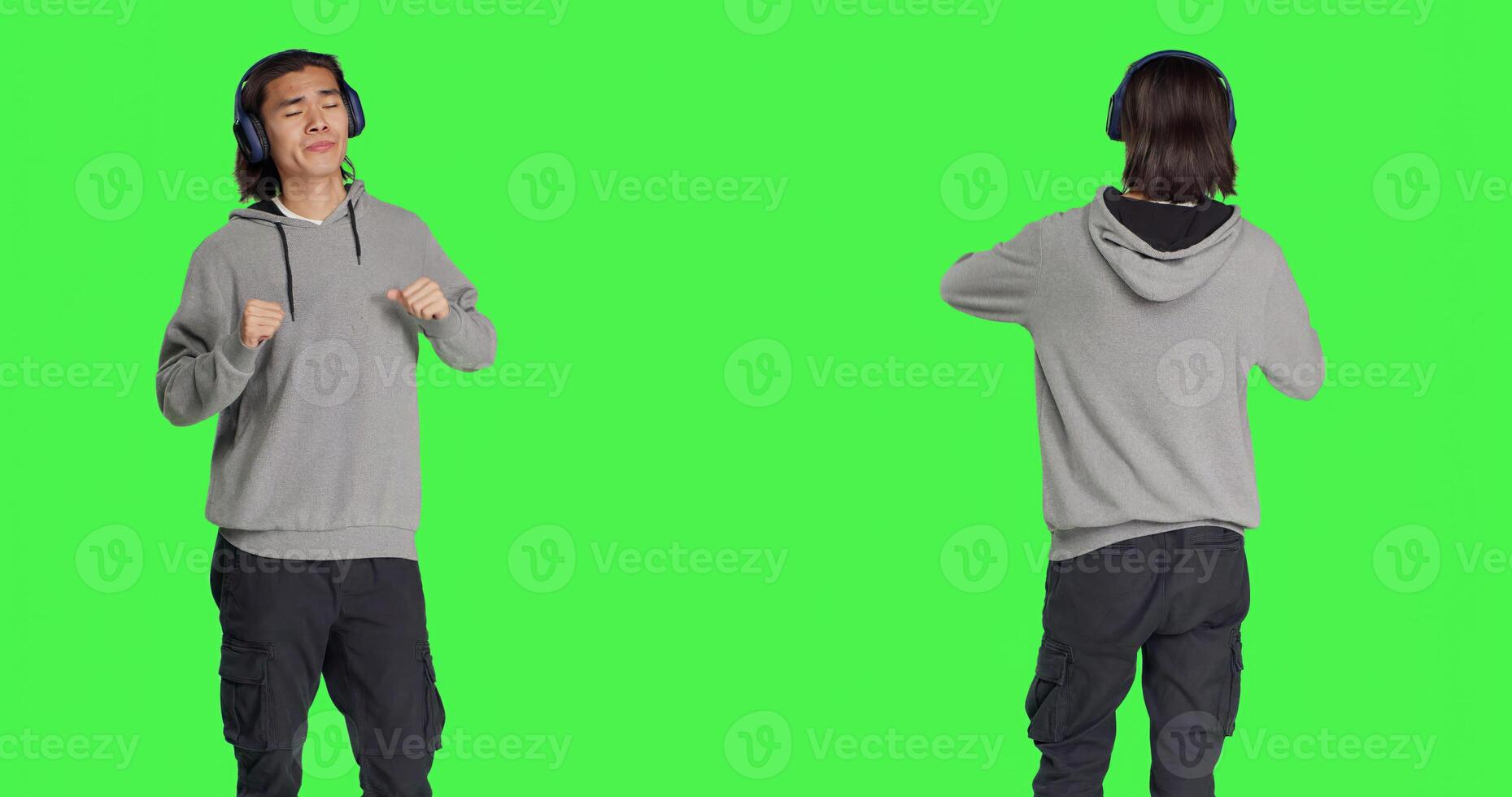 Positive guy does funky dance moves on camera, feeling groovy while he is listening to modern songs. Asian person smiling and enjoying music on headphones, dancing on greenscreen. photo