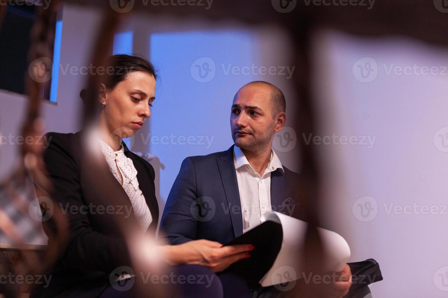 Employees on staircase late night afterhours tired from overtime, busy man and woman dealing with overwork and deadline. Colleague entrepreneur working late together in evening at corporate job sitting on staircase, explaining difficult finance project. photo