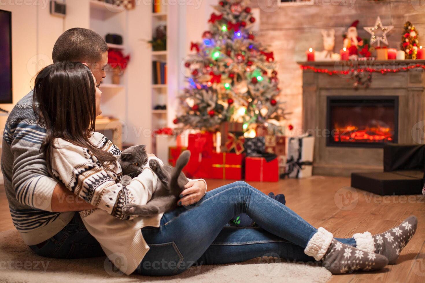 Couple in matching clothes and their scottish fold sitting together on the floor in front of fireplace celebrating christmas. photo