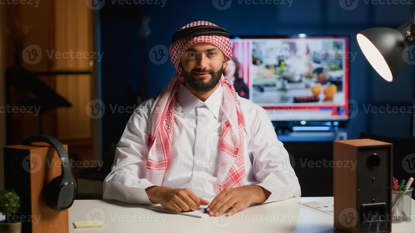 Portrait of smiling arab man paying attention in elearning webinar teleconference with teacher. Middle Eastern student in online videocall greeting tutor, listening to lesson while writing notes photo