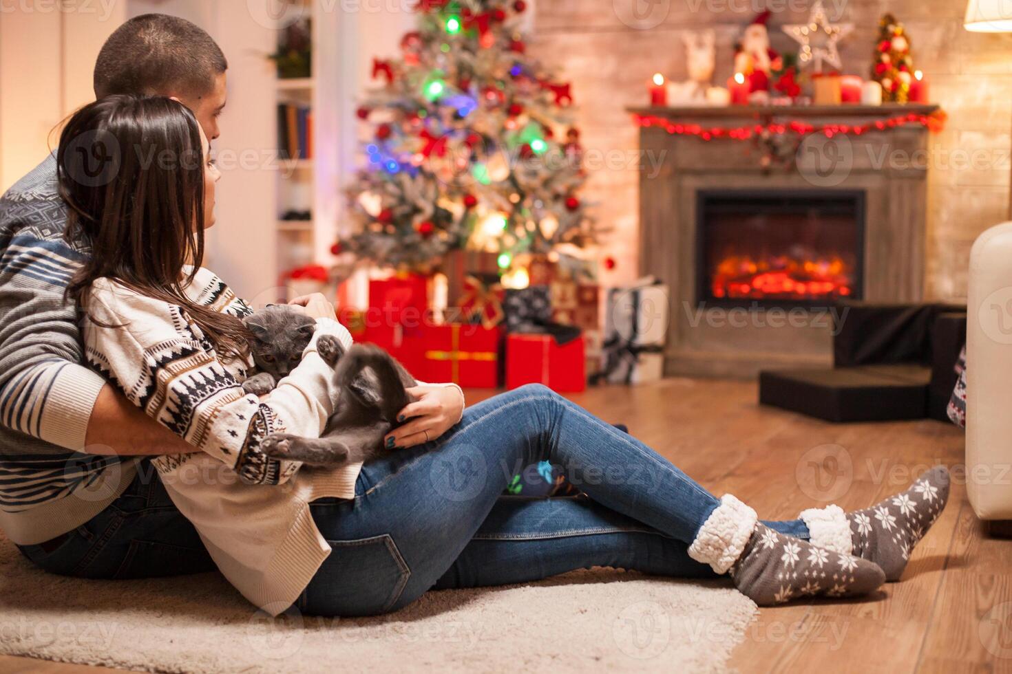Happy man laying on the floor with his girlfriend and scottish fold in front of fireplace celebrating christmas. photo