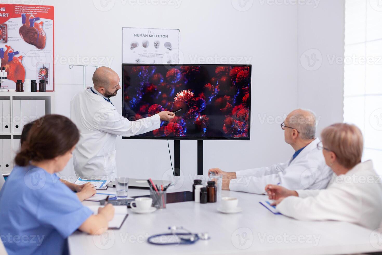 Virolog man specialist talking about coronavirus symptoms during virus presentation in front of practitioner doctors. Medical team of physicians planning vaccine against corona virus photo