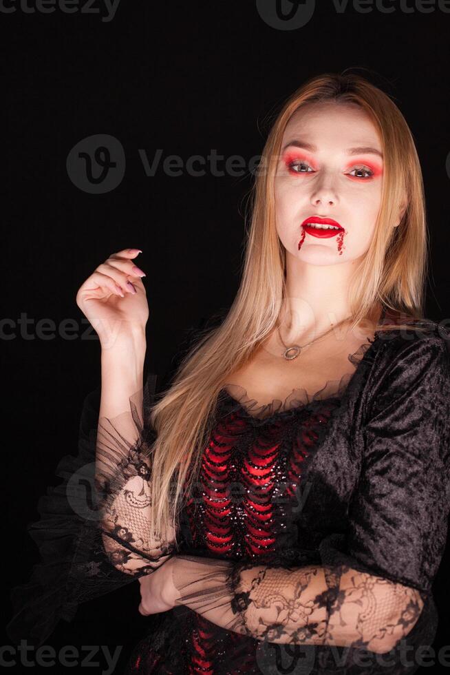 vampiro hermosa mujer con sangriento labios terminado negro antecedentes. Víspera de Todos los Santos traje. foto