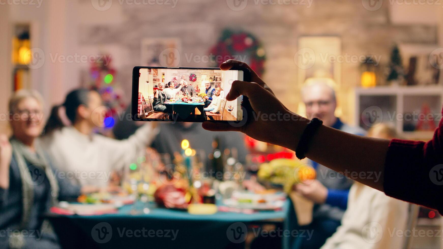Girl taking a family portrait with her phones while celebrating christmas. Traditional festive christmas dinner in multigenerational family. Enjoying xmas meal feast in decorated room. Big family reunion photo