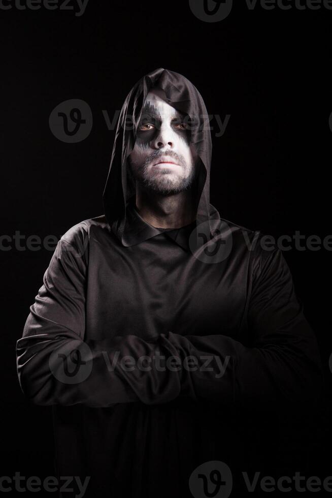 Portrait of grim reaper with hands crossed isolated over black background. Halloween costume. photo