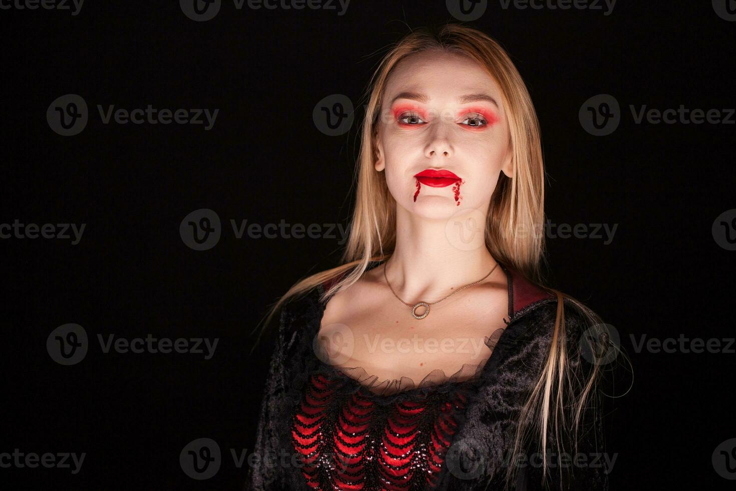 Evil vampire woman with blond hair over black background. Halloween outfit. photo