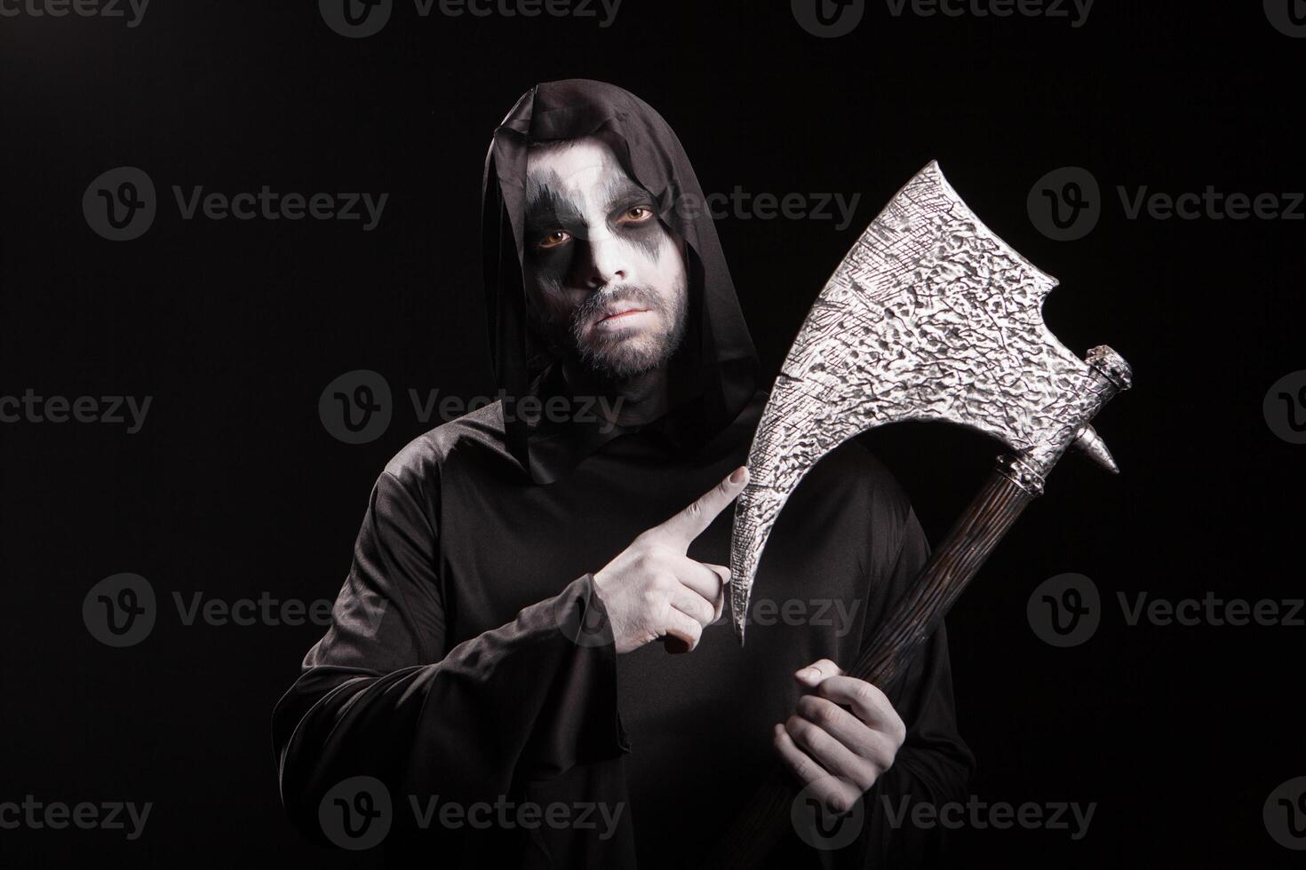 Dangerous scary man dressed up like grim reaper with an axe over black background. photo