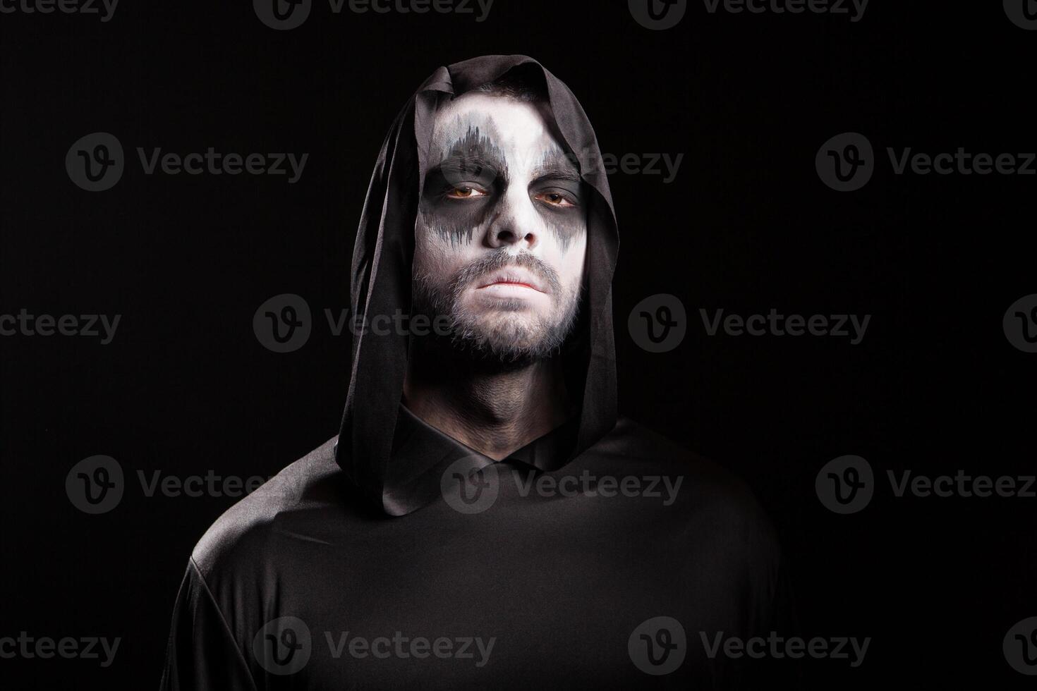 Man with creepy face dressed up like grim reaper over black background. photo