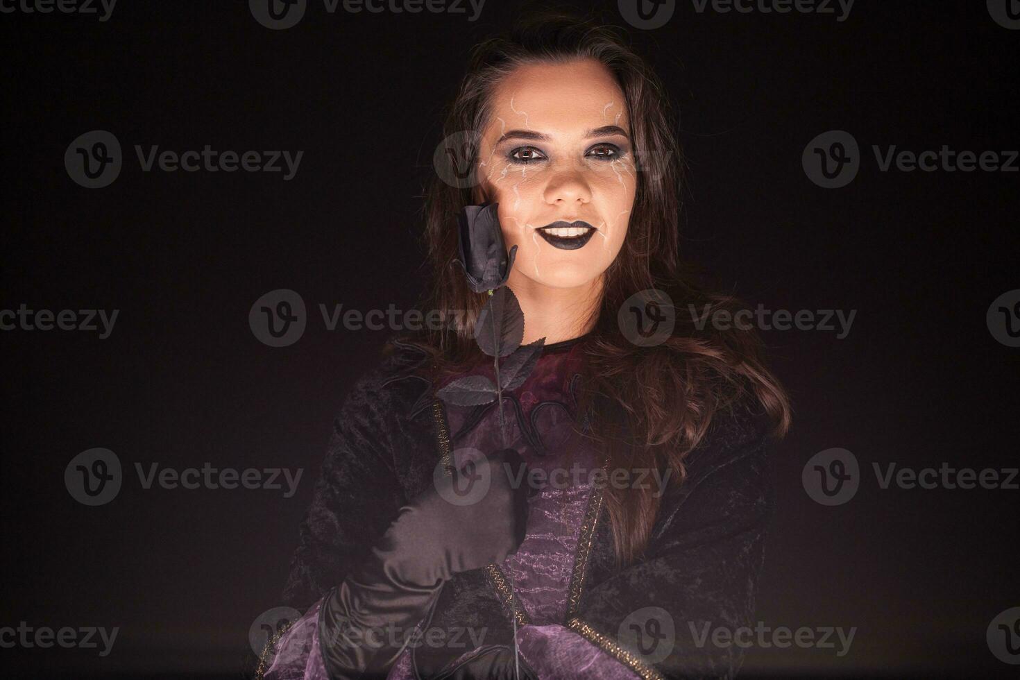 Evil and scary female witch over black background with a rose. Halloween costume. photo