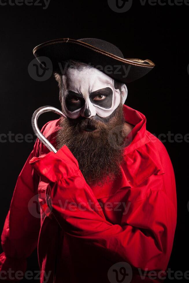 Man with long beard dressed up like a spooky pirate with a hook over black background. photo