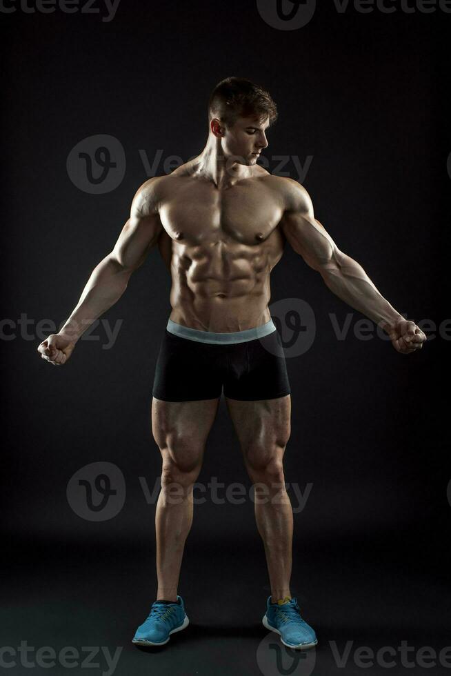 Muscular bodybuilder guy doing posing over black background photo