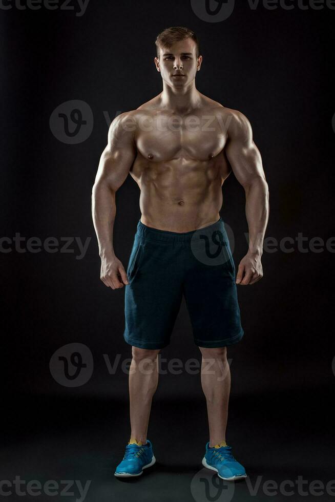 Muscular bodybuilder guy doing posing over black background photo